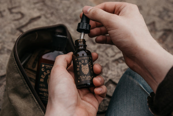 A man with beard oil and travel bag apply beard oil by Bawston & Tucker